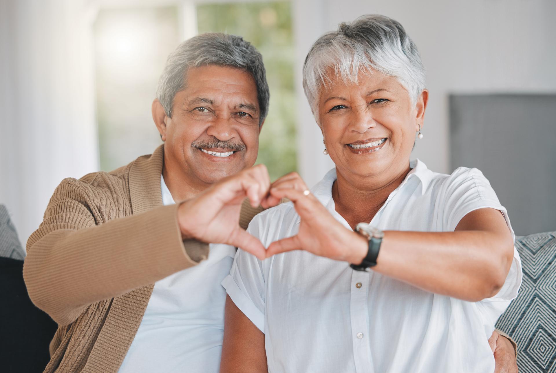 Portrait of a senior couple making a heart shape with their hands at home